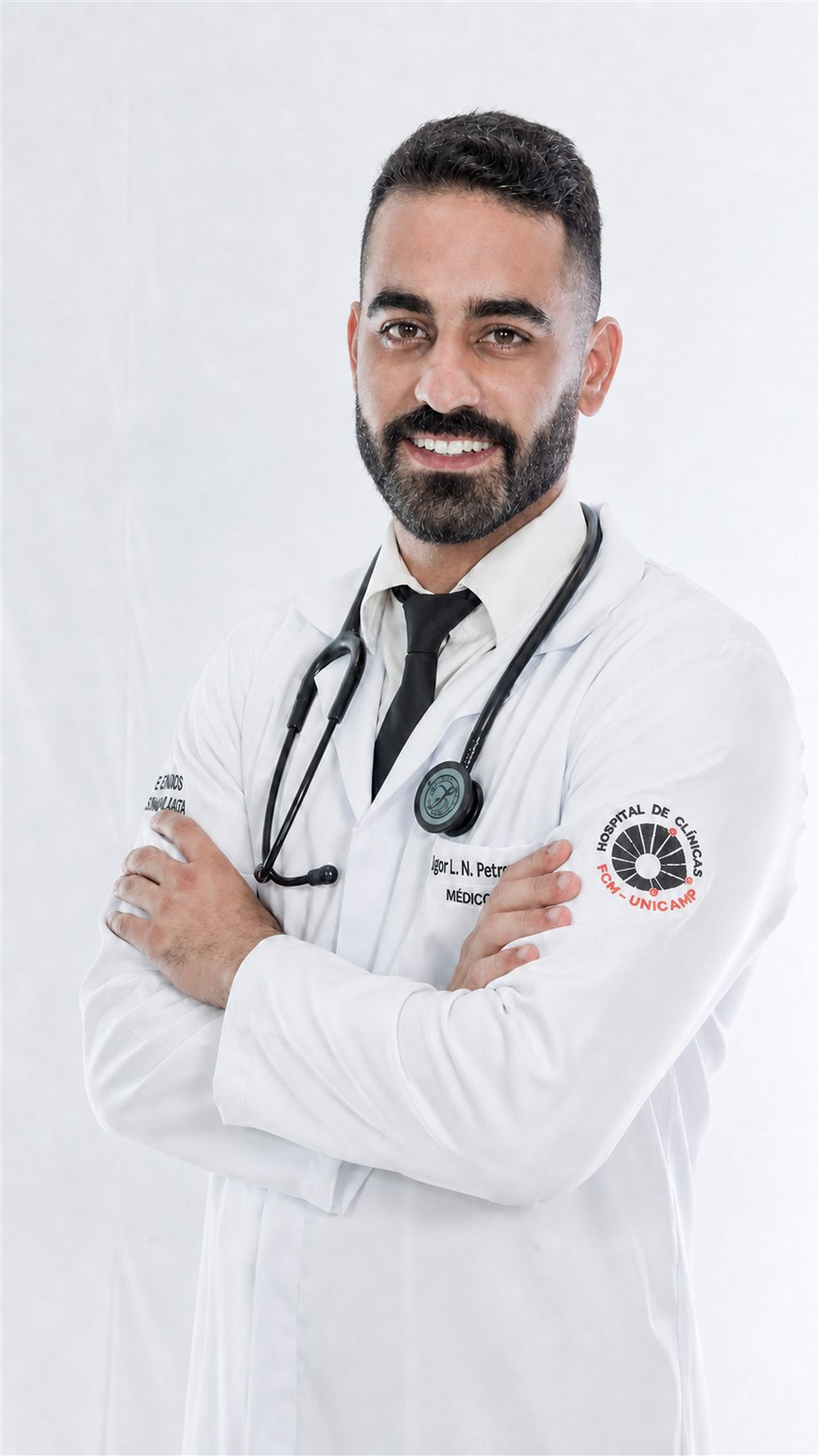 Dr. Igor L. N. Petrocino, de jaleco, sorrindo com os braços cruzados